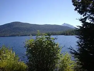 View across Alexander Lake, surrounded by forested terrain with distant mountains on the horizon under a partly cloudy sky.