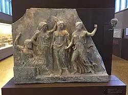 Ancient Greek carved relief in marble: Zeus, at left, sits enthroned; Leto is recognisably by her voluminous garments, while Apollo is bare-chested and the final female figure, clad in a thin tunic, gestures towards the right.