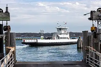 White hulled ferry with small superstructure pulls away from pier