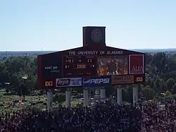 Large scoreboard in an American football stadium surrounded by crowded stands.