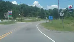 Roadway in a rural area with two gas station signs and trees in the background, and a "Arkansas Highway 100" sign in the foreground.