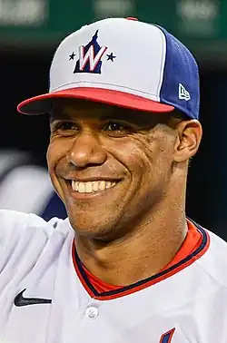 A man in a white shirt and cap smiling while looking to the left of the image.