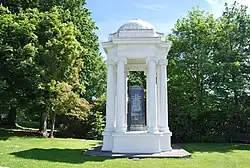 A white monument sheltering a black inscribed obelisk