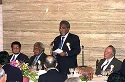 Mekere Morauta standing up and speaking from a seat at a table with other sitting alongside