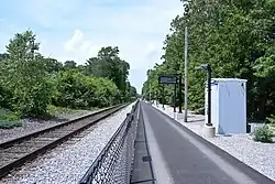 An asphalt walkway next to a railway track, with a fence between