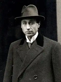 A middle-aged man in a suit and a brimmed cap with a dressy winter coat