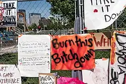 Different protest signs hung on a fence. One of them reads: "Burn this Bitch down".