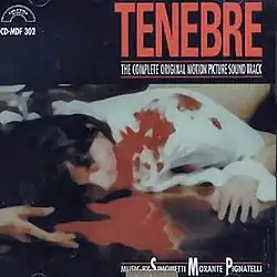 A figure with dark hair and wearing a white shirt prone in a pool of blood. Above, "TENEBRE".
