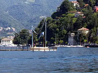 Tall, abstract stainless steel sculpture consisting of two curving forms reaching upwards, set against a lake and mountains.