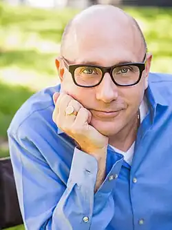 Portrait of Garson wearing a blue dress shirt and leaning on his hand