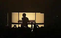 Photo of from behind of a silhouetted De Rosnay playing a keyboard