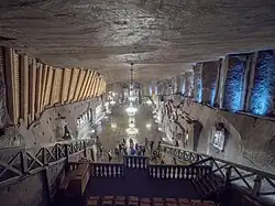 Large room with lamps hanging from the ceiling and sculptures or reliefs along the walls.