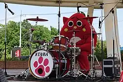 A red costumed mascot playing a drum kit.