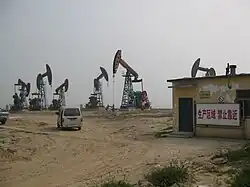 A number of orange and blue oil wells on yellow dusty land