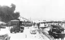 A twin-engine airliner with three fins parked on ramp while being serviced, with mobile staircases nearby.
