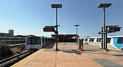 Two metro trains at an open-air platform. A commuter train is visible at far left.