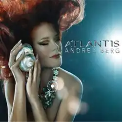 A red-haired woman underwater with her eyes closed. She is wearing a shiny pearl necklace. She is holding a shellfish against her cheek. The words "Andrea Berg Atlantis" are written in silver on the right.