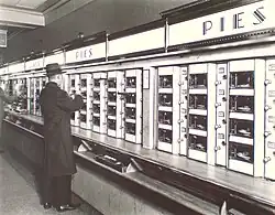 A man stands in front of rows of glassed-in shelves, to choose which food he wants to buy