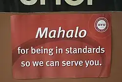 Photo of a sign on the wall that reads "Mahalo for being in standards so we can serve you".