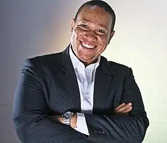 Christian Ngan, a Cameroonian entrepreneur, smiling confidently in a dark pinstripe suit with arms crossed, photographed in Yaoundé in November 2014.