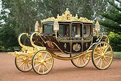 A very ornate coach, black with gold trim, a coat of arms on the door