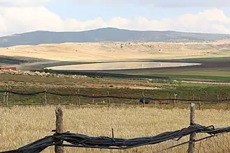 A field surrounded by a split-rail fence, with a body of water visible in the distance.