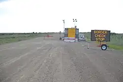 an electronic sign that says "Border Check Stop" on a gravel road.