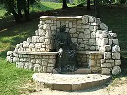 Gray outdoor statue of seated man, surrounded by white stone alcove