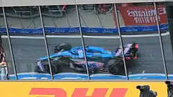 Fernando Alonso driving the Alpine A522 at the 2022 Austrian Grand Prix, viewed in a window's reflection