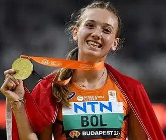 Photo of Femke Bol with a flag draped over her shoulders and holding a gold medal