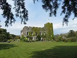 a stone building covered in greenery, with grass in the foreground