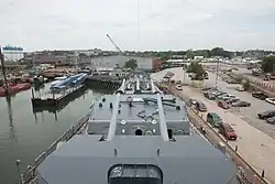 Looking down the front of a ship towards the yard, with artillery guns in the foreground and the buildings of the yard in the background