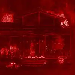 Cover art for Dolido Pero No Arrepentido, which is an red-tinted image of a house on fire.