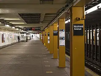 An underground train station with outer platforms. A pillar bisecting the image is painted a burnt yellow.