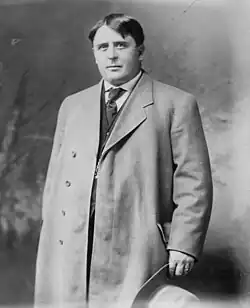 Jack Abernathy, standing in coat holding hat