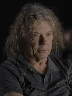 close-up of Jerry Harrison wearing a dark sleeveless top, looking left of camera with a set facial expression