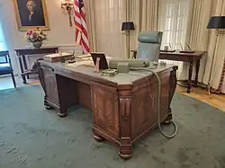 the desk viewed from slightly above showing the green top and the rest of the replica Oval Office behind it.
