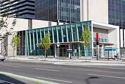 Photo of a largely completed underground light rail station in glass and white panelling with orange accents.