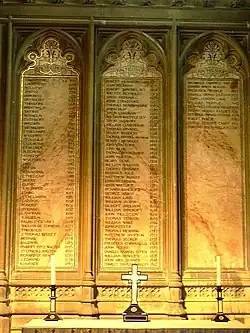 Three plaques on a wall, inscribed with the lists of the archbishops. In front of the plaques is a table with two candlesticks flanking an upright cross.