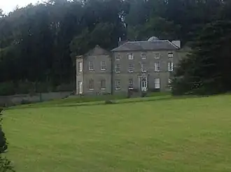 a grass lawn in front of a large house with trees in the background