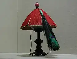 A red conical hat with a large peacock feather, on a stand