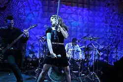 three musicians (two male with guitars, one female on vocals) on stage