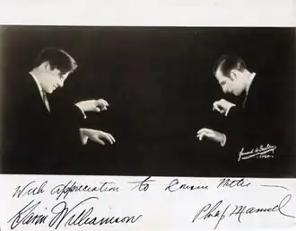 Two men opposite, hands raised above invisible keyboards, signatures below in bottom right; another unidentified signature in the bottom right of the picture.