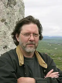 Head and shoulders photo of a man in a jacket with a beard and moustache looking into the camera.