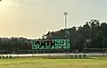 Tennis courts surrounded by chain-link fencing hold a green "PANTHERS" banner with a black panther outline walking through the letters; trees are in the background and grass in the foreground