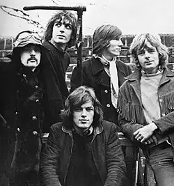 A black-and-white photo of the five band members standing in front of a brick wall in 1968.