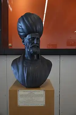 A photograph of a bust, stored at a museum, of a bearded and turbaned man