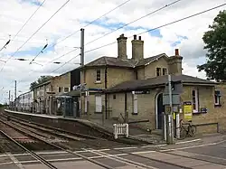 A large yellow-brick building that is a mix of one and two storeys.The building has one side on a railway platform and the other on the street, and the photo is taken from a level crossing looking at the building and platform above.