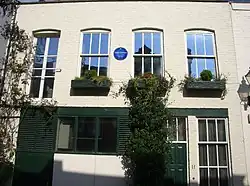 exterior of cream painted mews house, with blue plaque on front wall
