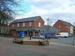 Black cradle with curved rockers at both ends mounted on a raised brick plinth having public seating benches around set in a paved open area